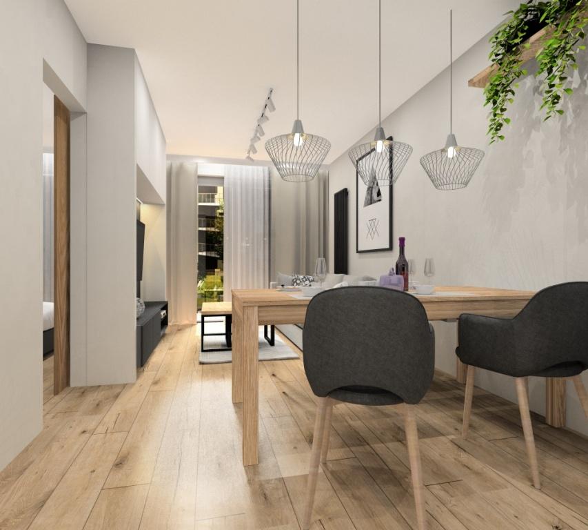 Salon, projekt mieszkania 43m2, mieszkanie dwupokojowe, zabudowa RTV w kolorze białym, drewno ciepły odcień, grafitowy, beżowo-szara sofa, białe lampy, plakat nad sofą złoty, czarny, stolik kawowy drewniany